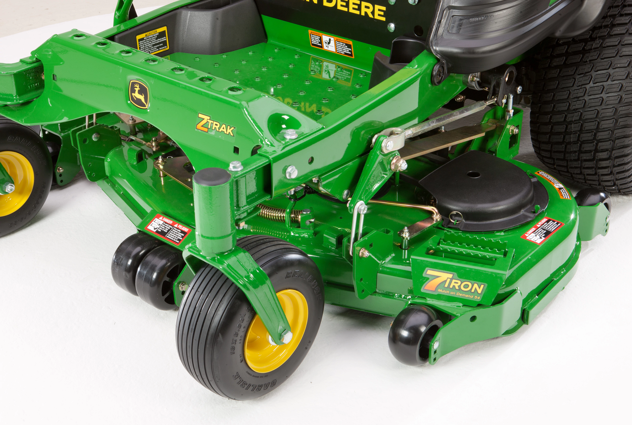 Close-up of a ZTrak mower deck showing the front caster wheel, mower deck housing, anti‑scalp wheels, linkage components, and labels on the deck surface
