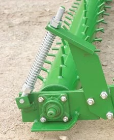 Close-up of a mounting bracket with a visible coil spring, bolted cylindrical bearing housing, and evenly spaced metal spikes along the top.